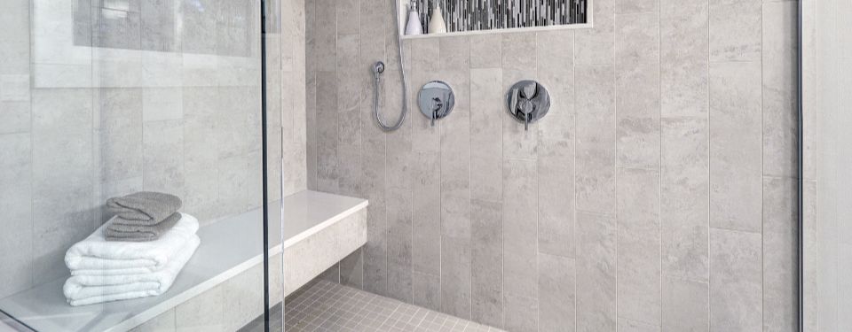Walk in shower with grey tile and towels placed on shower bench.