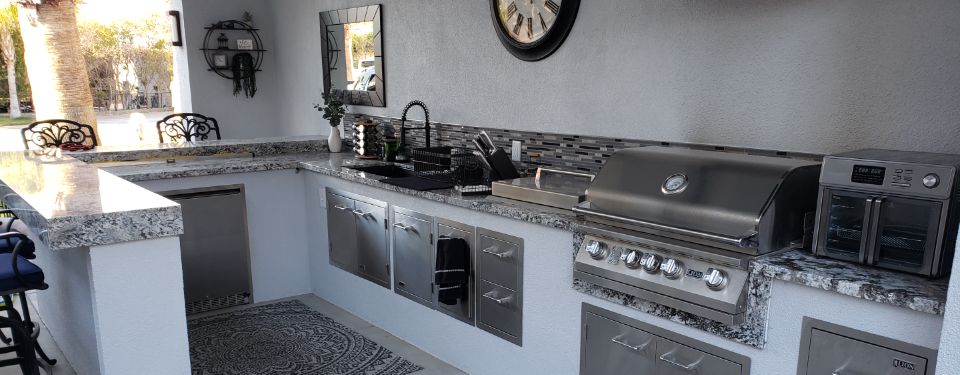 Outdoor kitchen at a home, featuring a grill, sink, and dishwasher, all made with a striking stainless steel design